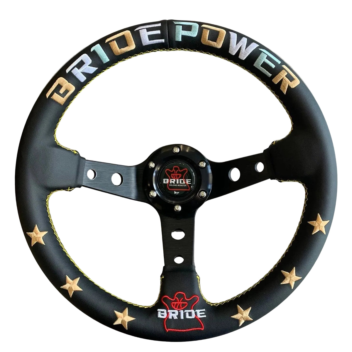 A black leather-wrapped car steering wheel with gold star accents, yellow stitching, and 'BRIDE POWER' lettering in gold, blue, and white on the rim. The center cap features the Bride logo.