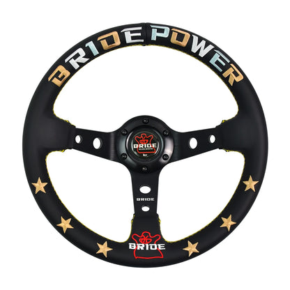 A black three-spoke steering wheel cover by Bride Power, featuring gold stars and gold, blue, and white lettering on the rim, with a red and gold center cap.