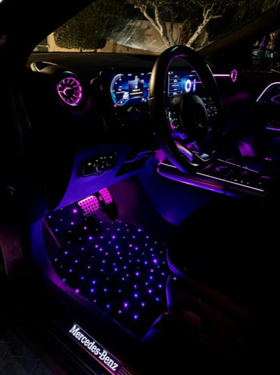 Car interior with neon lights, galaxyglow starlight floor mats and a Mercedes-Benz logo on a mat.