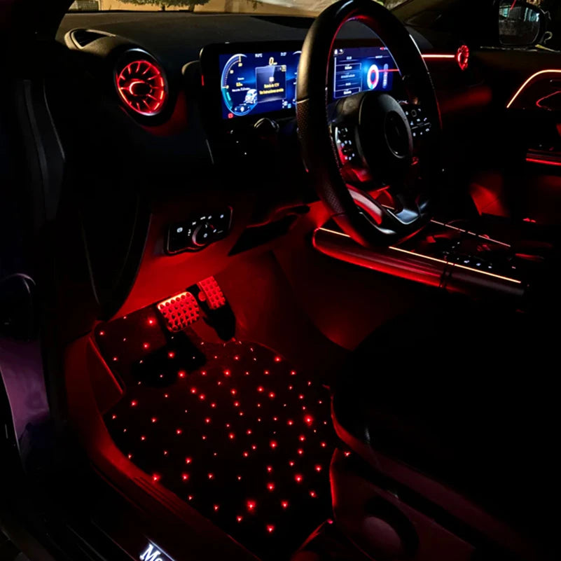 Car interior with illuminated dashboard and red LED starlight floor mat lights on the floor.