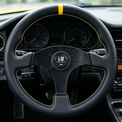 A close-up of a black leather car steering wheel with yellow contrast stitching and a yellow accent stripe near the top. The center has a black multi-spoke wheel design with a circular logo badge.