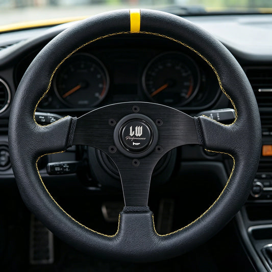 A close-up of a black leather car steering wheel with yellow contrast stitching and a yellow accent stripe near the top. The center has a black multi-spoke wheel design with a circular logo badge.