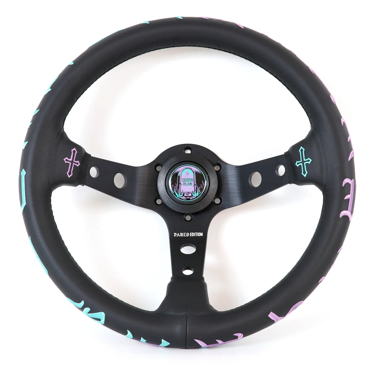 A black leather-wrapped car steering wheel with a matching black three-spoke center, featuring pastel pink and light blue decorative accents along the rim and a colorful iridescent center cap, shown on a white background.