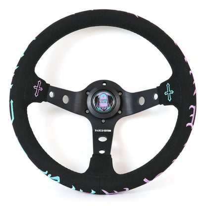 A black suede-wrapped steering wheel with a black metal center and spindles, decorated with light blue and pink cross accents and pink lettering on the outer rim.