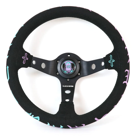 A black suede-wrapped steering wheel with a black metal center and spindles, decorated with light blue and pink cross accents and pink lettering on the outer rim.