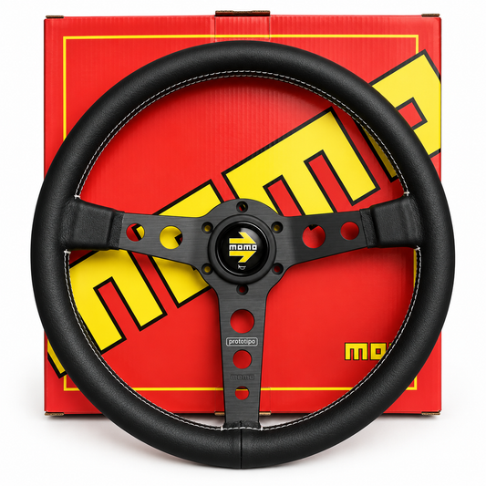 A black leather-wrapped steering wheel with a black three-spoke metal center, shown in front of its red and yellow Momo brand packaging box.