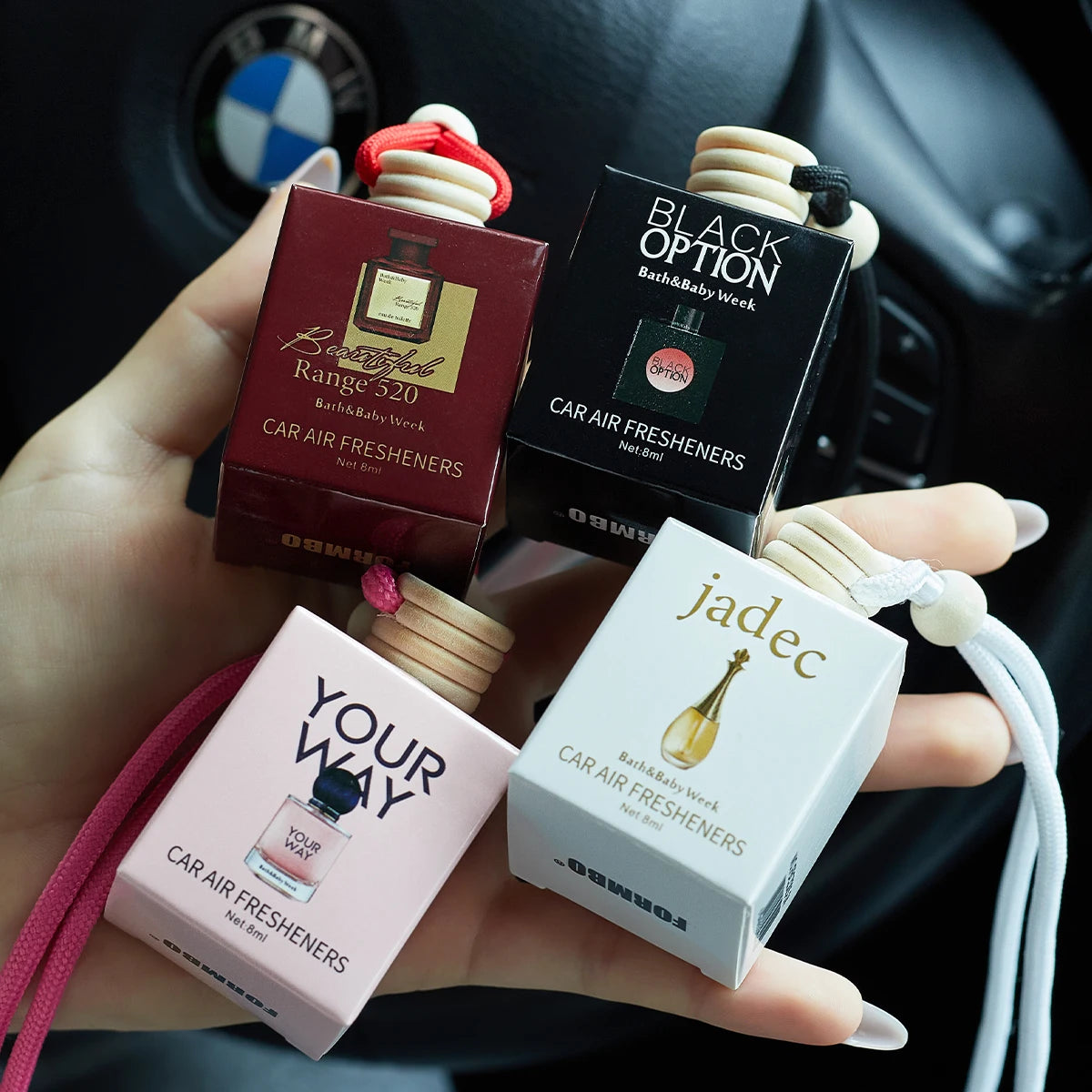 Four car air freshener boxes from different brands held in a hand with a car interior background.