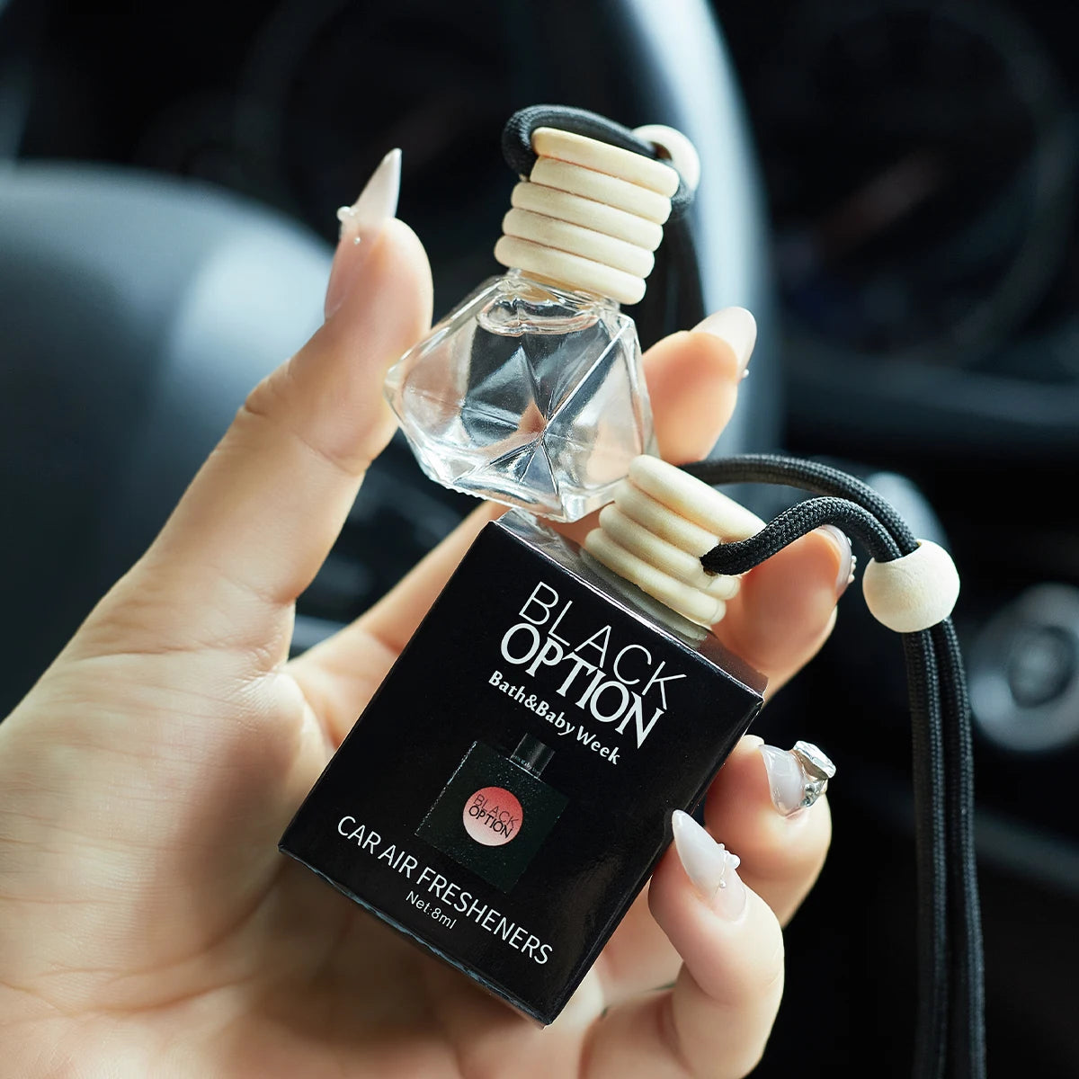 Hand holding a car air freshener with 'Black Option' branding.