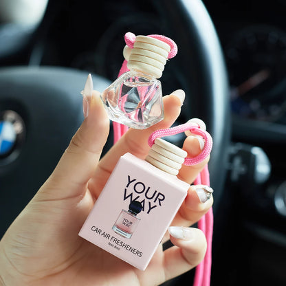 Hand holding a car air freshener labeled 'Your Way' in front of a car interior.